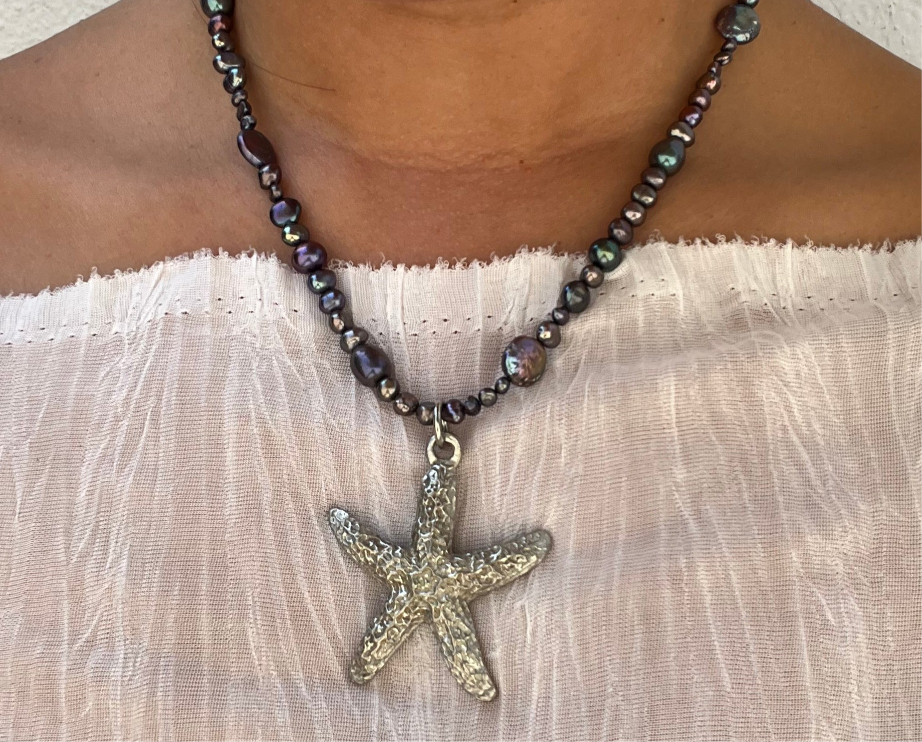 Shop Querida 17 inch long necklace inspired by night walks by the beach stargazing and appreciation of nature made with freshwater pearls that have dark purple, green, black hues, vintage second hand sourced stainless steel starfish Beachy mystical bohemian fairy 